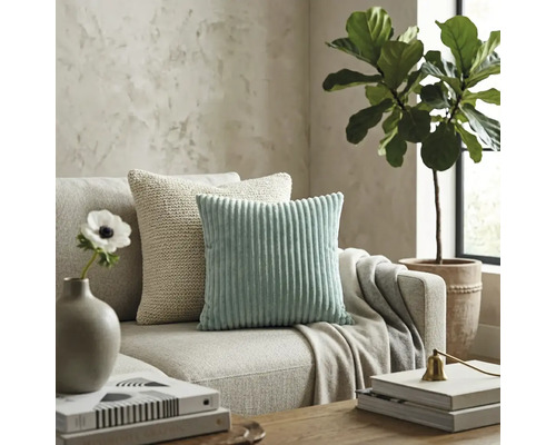 Sufragerie modernă cu o pernă decorativă din catifea raiată verde mentă și o pernă tricotată bej pe o canapea din material textil neutru.