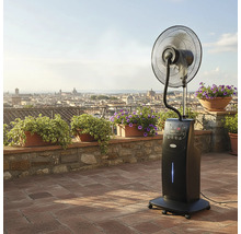 Ventilator cu picior negru cu funcție de pulverizare pe o terasă cu plante și vedere panoramică asupra orașului.