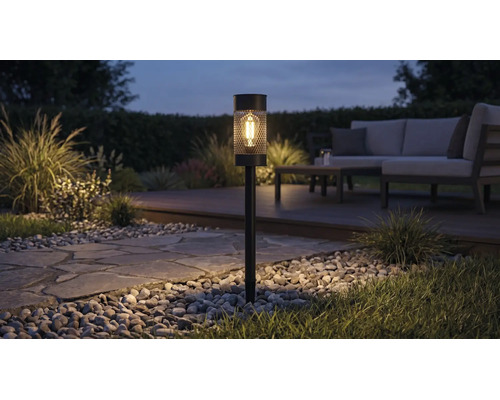 Lampă solară de grădină cu bec LED și design tip plasă, iluminând o alee de grădină noaptea lângă un set de mobilier de grădină.