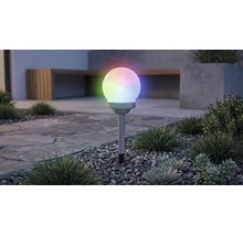 Lampă solară de grădină în formă de glob cu iluminare RGB multicoloră, pe un țăruș într-un strat de pietriș cu plante.