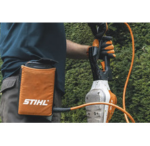 Persoană cu borsetă pentru acumulator Stihl și cablu de conectare la o foarfecă de tuns gard viu în timpul lucrului.