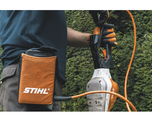 Persoană cu borsetă pentru acumulator Stihl și cablu de conectare la o foarfecă de tuns gard viu în timpul lucrului.
