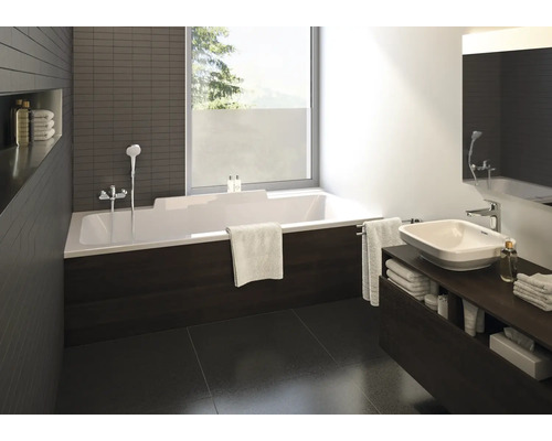 Baie modernă cu cadă dreptunghiulară albă, mască cu aspect de lemn închis la culoare, lavoar pe blat pe mobilier închis și fereastră mare.