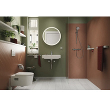 Baie modernă cu vas WC suspendat, lavoar, oglindă rotundă, zonă de duș, rafturi și plante de interior.