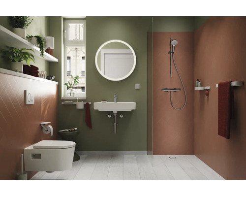 Baie modernă cu vas WC suspendat, lavoar, oglindă rotundă, zonă de duș, rafturi și plante de interior.