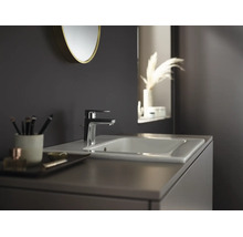 Scenă de baie modernă cu o baterie de lavoar elegantă pe un lavoar din ceramică, o oglindă rotundă și un mobilier de lavoar.