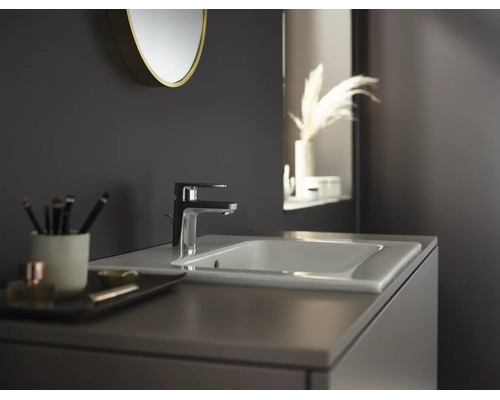 Scenă de baie modernă cu o baterie de lavoar elegantă pe un lavoar din ceramică, o oglindă rotundă și un mobilier de lavoar.