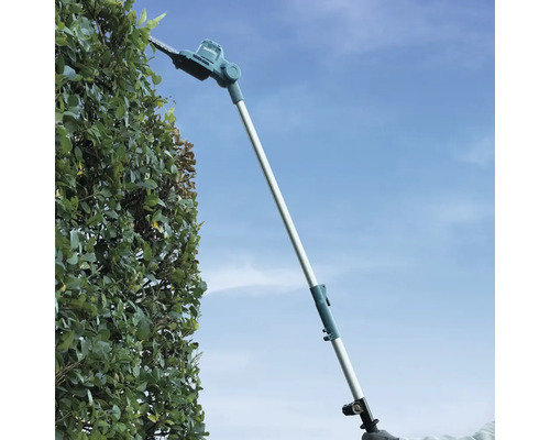 Trimmer telescopic pentru gard viu Makita tăind un gard viu înalt în exterior.