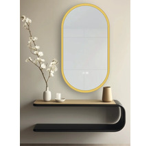 Oglindă de perete LED ovală cu ramă aurie, montată deasupra unei console de perete moderne cu decorațiuni într-o cameră luminoasă și ordonată.