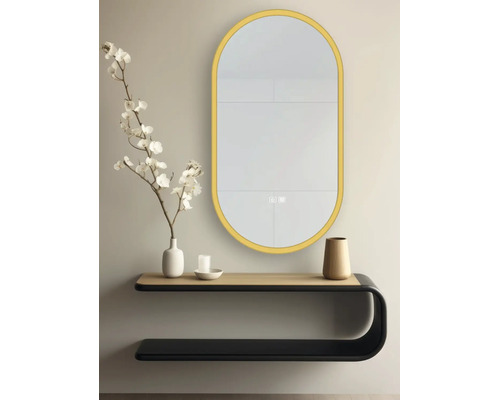 Oglindă de perete LED ovală cu ramă aurie, montată deasupra unei console de perete moderne cu decorațiuni într-o cameră luminoasă și ordonată.