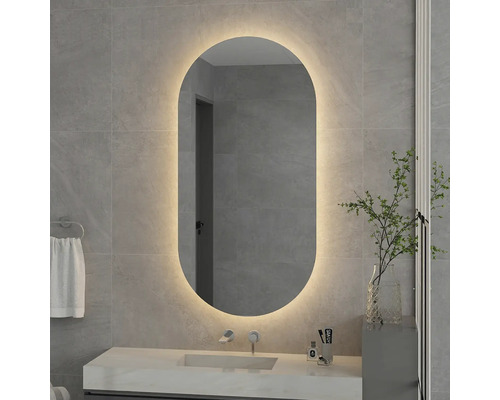 Oglindă de baie ovală cu iluminare din spate cu LED pe un perete placat cu faianță deasupra unei chiuvete cu baterie.