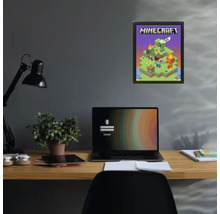 Poster Minecraft într-o ramă neagră pe un perete închis la culoare, deasupra unui birou cu un laptop și o plantă.