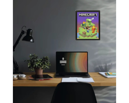 Poster Minecraft într-o ramă neagră pe un perete închis la culoare, deasupra unui birou cu un laptop și o plantă.