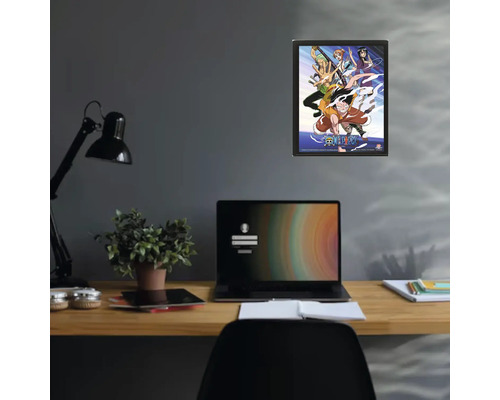 Poster One Piece înrămat pe un perete deasupra unui birou cu laptop și plantă de apartament.