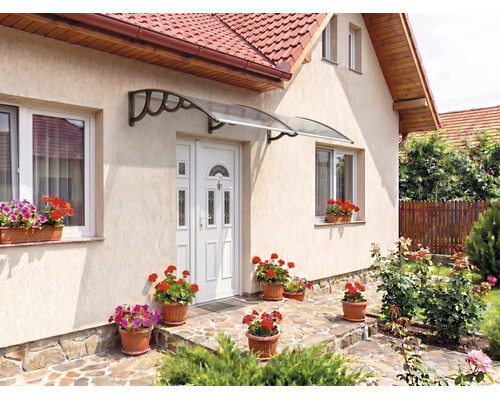 Copertină transparentă deasupra unei uși de intrare albe pe o fațadă deschisă la culoare cu jardiniere și terasă din piatră.