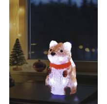 Figurină luminoasă din acril în formă de veveriță cu fular roșu pe o masă, decorațiune de Crăciun cu brad în fundal.