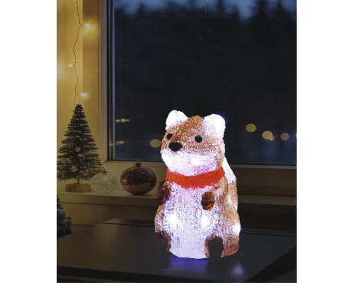 Figurină luminoasă din acril în formă de veveriță cu fular roșu pe o masă, decorațiune de Crăciun cu brad în fundal.