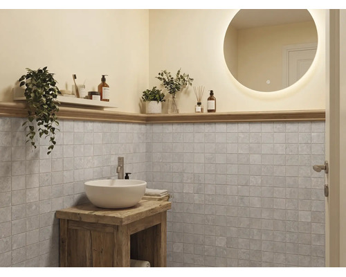 Baie modernă cu oglindă rotundă iluminată, lavoar alb pe mobilier din lemn rustic și faianță pătrată gri.