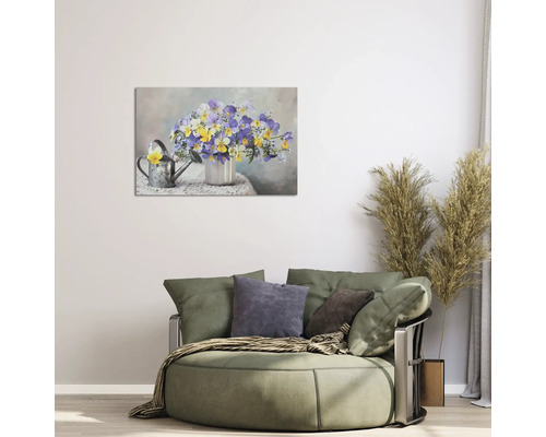 Tablou pe pânză cu flori pe un perete deschis deasupra unui fotoliu rotund mare cu perne într-o sufragerie luminoasă.