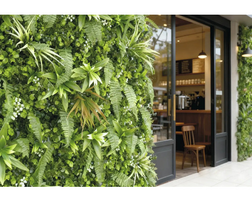 Grădină verticală cu ferigi și plante artificiale lângă o intrare de cafenea din sticlă cu cadru negru.