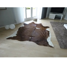 Covor din piele de vacă cu formă naturală într-o cameră de zi modernă și luminoasă, cu parchet deschis la culoare.
