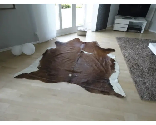 Covor din piele de vacă cu formă naturală într-o cameră de zi modernă și luminoasă, cu parchet deschis la culoare.