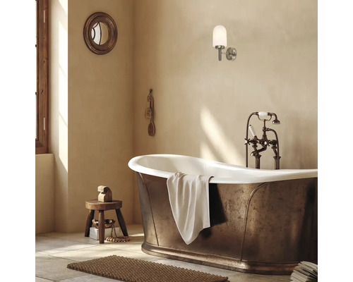 Cadă de sine stătătoare cu aspect de bronz, baterie nostalgică și aplică de perete modernă într-o baie luminoasă.