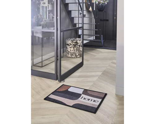 Hol modern cu un preș cu model geometric și inscripția home pe o podea în stil brăduț, lângă o ușă de sticlă.