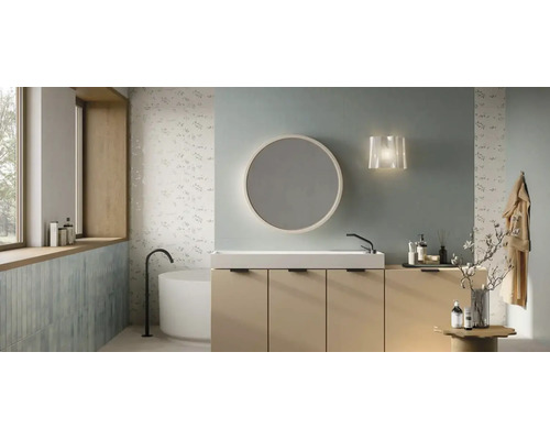 Baie modernă cu mască de lavoar bej, lavoar alb, oglindă rotundă și cadă de sine stătătoare în fața plăcilor ceramice cu model floral.
