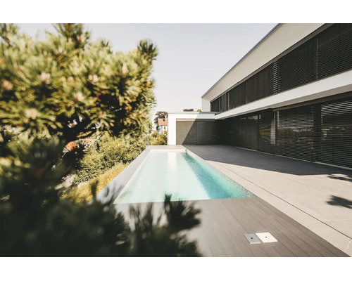 Casă modernă albă cu jaluzele exterioare negre, piscină dreptunghiulară îngustă și terasă spațioasă cu plăci de piatră gri.