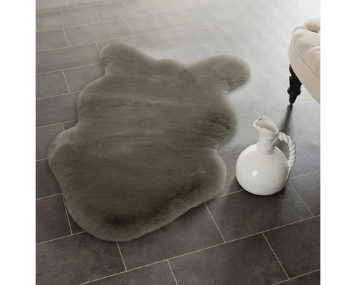 Imitație moale de blană de miel în formă de animal pe o podea cu gresie lângă un urcior din ceramică.