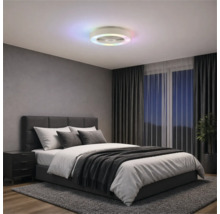 Ventilator de tavan modern cu inel LED colorat într-un dormitor cu pat tapițat gri, perdele închise la culoare și covor.