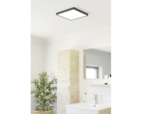 Baie luminoasă cu plafonieră LED pătrată, chiuvetă modernă, dulap înalt cu aspect de lemn și plantă de interior.