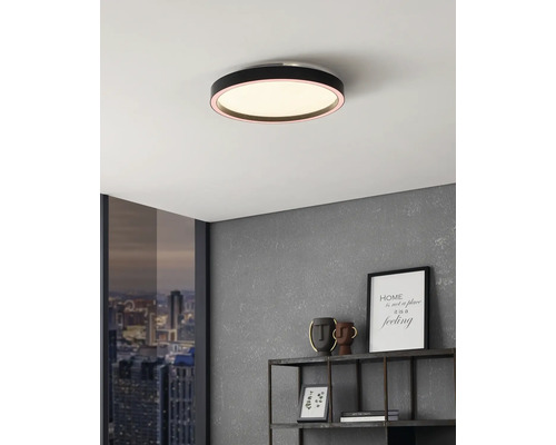 Plafonieră LED rotundă și plată, neagră, montată pe un tavan alb într-un decor modern cu perete gri și raft metalic.