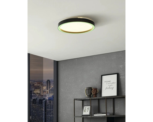 Plafonieră LED rotundă modernă cu cadru negru și inel luminos verde într-o cameră cu perete gri și raft metalic.