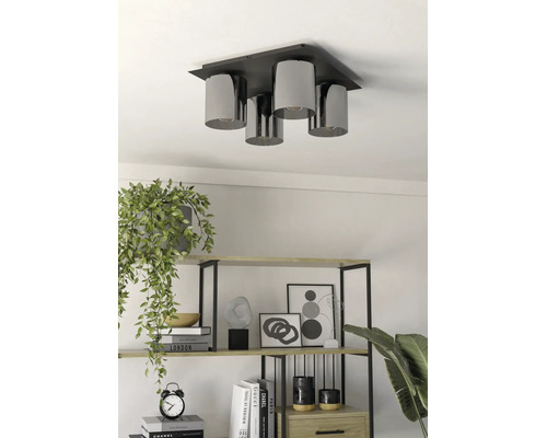 Plafonieră modernă cu 4 surse de lumină și abajururi cilindrice deasupra unui raft cu decorațiuni și plante.