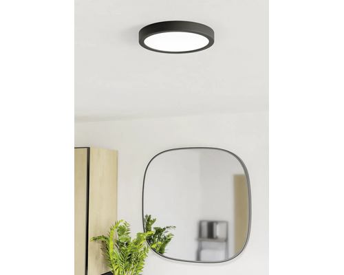 Plafonieră LED rotundă modernă, de culoare neagră, într-o cameră luminoasă, deasupra unei oglinzi și a unei plante.