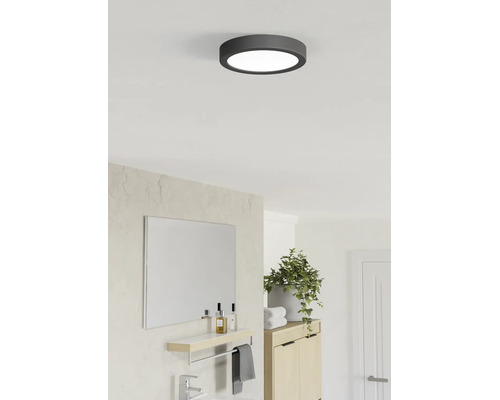 Plafonieră LED rotundă cu cadru închis la culoare într-o baie modernă și luminoasă, cu oglindă, plantă verde și dulap din lemn.