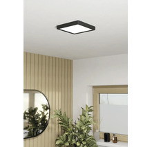 Plafonieră LED pătrată, neagră, într-o cameră luminoasă cu perete din panouri de lemn, oglindă și plantă de interior.