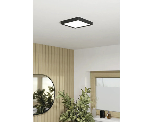 Plafonieră LED pătrată, neagră, într-o cameră luminoasă cu perete din panouri de lemn, oglindă și plantă de interior.