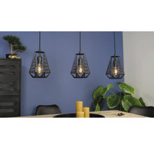 Trei pendule negre cu design tip colivie deasupra unei mese din lemn într-o cameră mobilată modern, cu plante.