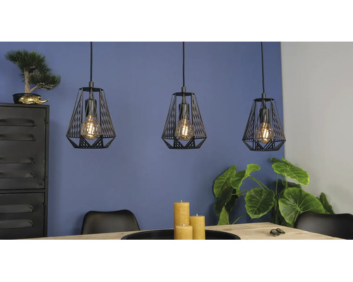 Trei pendule negre cu design tip colivie deasupra unei mese din lemn într-o cameră mobilată modern, cu plante.