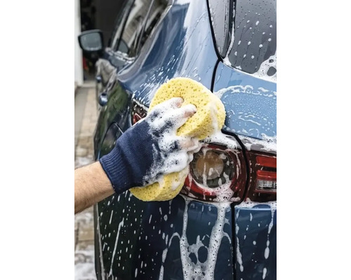 Curățarea unei mașini cu un burete auto mare, poros și spumă albă de curățare.