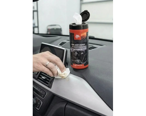 Mână care curăță un bord de mașină cu un șervețel umed Dirt Devil Car Wet Wipe pentru interior, lângă recipientul cu 40 bucăți.