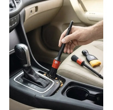 O mână folosește o pensulă pentru detailing auto pentru a curăța consola centrală și maneta schimbătorului de viteze în interiorul mașinii.