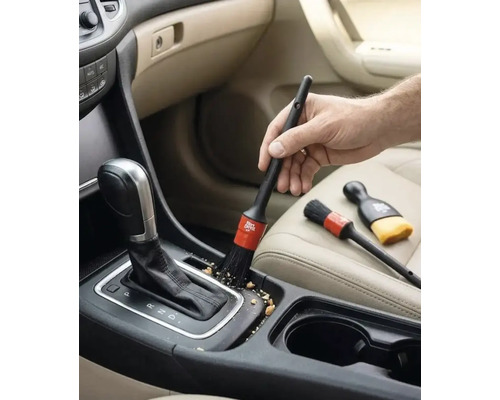 O mână folosește o pensulă pentru detailing auto pentru a curăța consola centrală și maneta schimbătorului de viteze în interiorul mașinii.