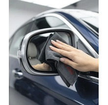 O mână curăță oglinda laterală a unei mașini cu o lavetă din microfibră pentru curățarea auto.