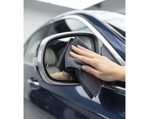 O mână curăță oglinda laterală a unei mașini cu o lavetă din microfibră pentru curățarea auto.