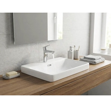 Baie modernă cu un lavoar pe blat din ceramică albă pe o placă de lemn, baterie cromată și o oglindă.