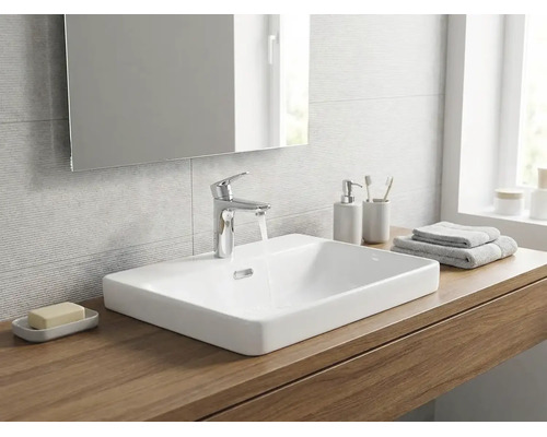 Baie modernă cu un lavoar pe blat din ceramică albă pe o placă de lemn, baterie cromată și o oglindă.